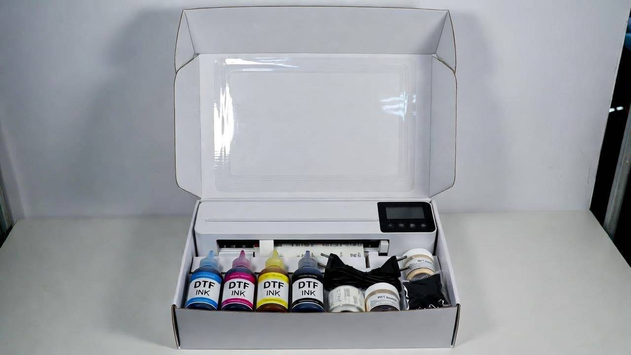 DTF printer unboxing showing printer unit, power cables, ink bottles, film rolls, and accessories