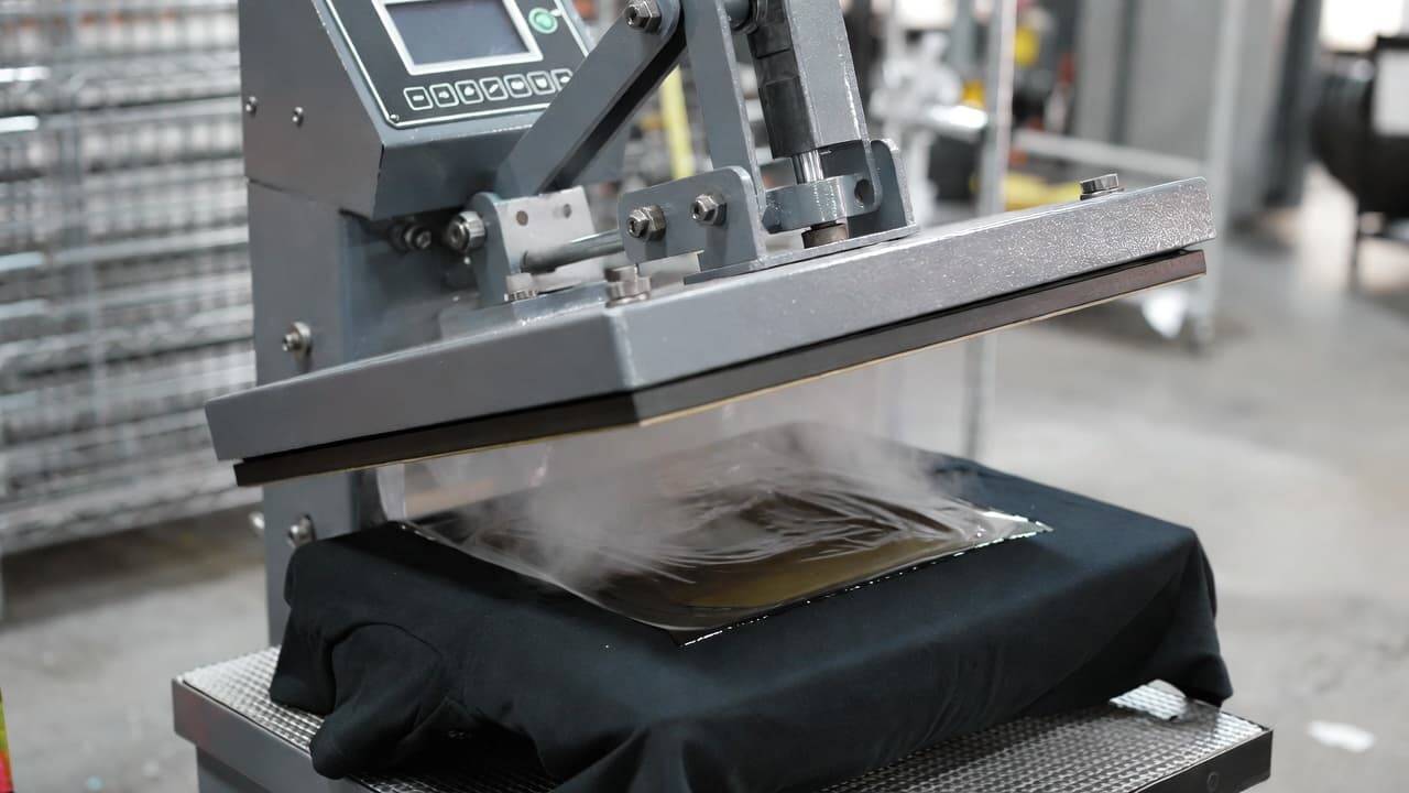 Heat press machine transferring DTF design from film onto black t-shirt with high pressure and temperature