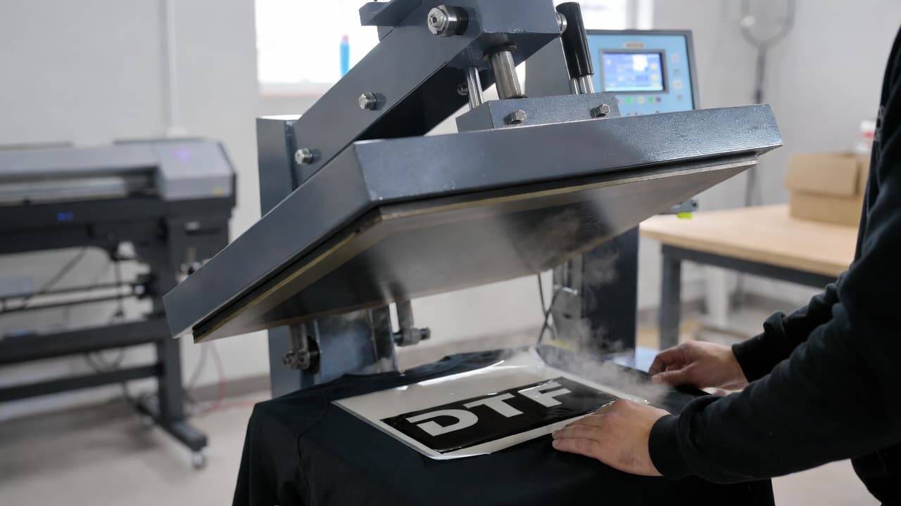 Heat press machine transferring DTF print onto black t-shirt